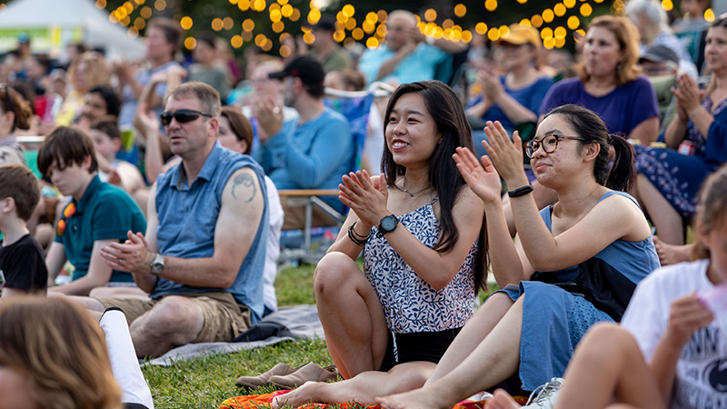 Young Friends members smiling and clapping while at an outdoor concert.